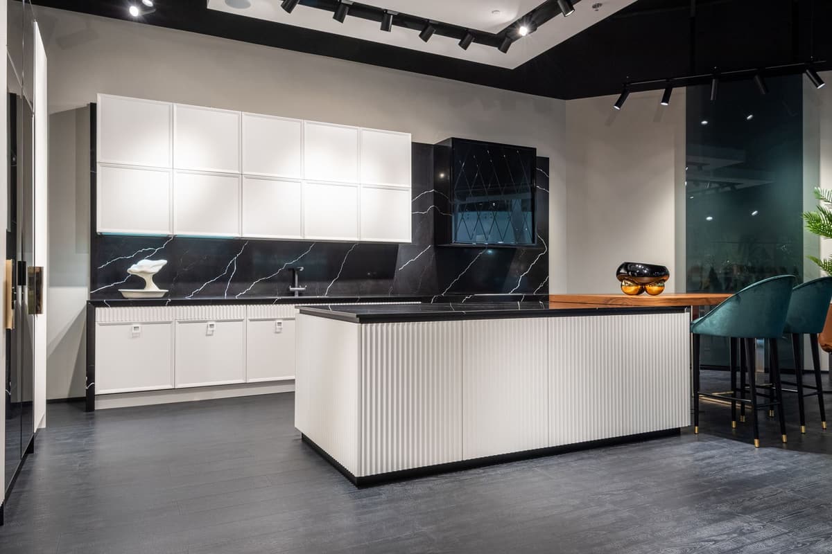 Après travaux : cuisine moderne blanche avec îlot central, plan de travail noir et électroménager encastré