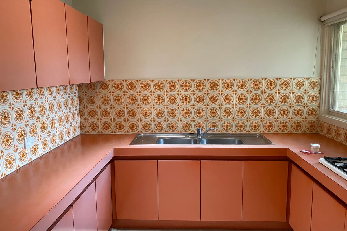 Avant travaux : cuisine des années 1970 aux façades orange et crédence à motifs, évier inox deux bacs