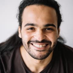 Portrait carré d'un homme barbu aux cheveux longs, souriant sur fond clair