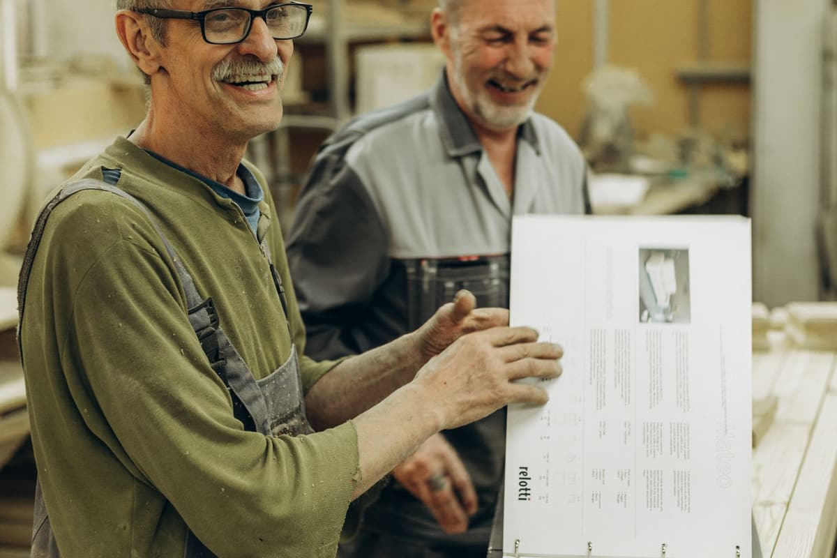 Deux artisans expérimentés rient en consultant un dossier technique dans leur atelier