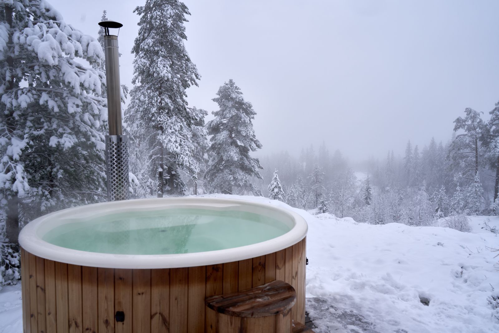 Bain nordique en bois fumant, entouré de sapins couverts de neige