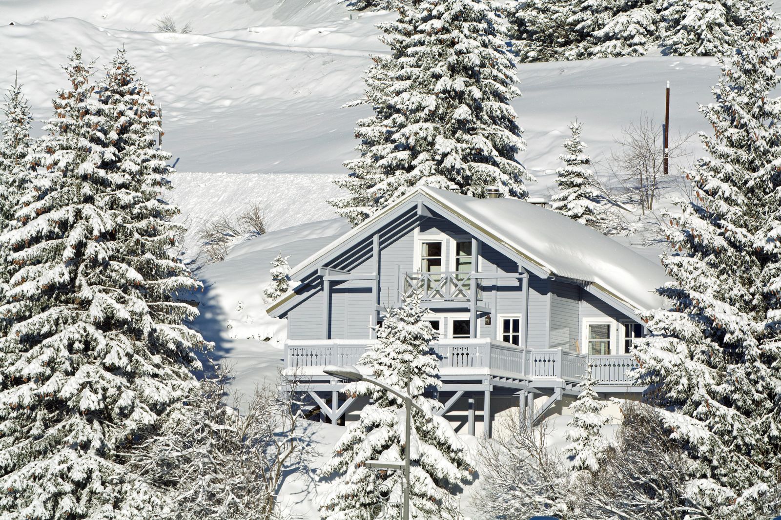 Chalet en bois gris-bleu couvert de neige, entouré de sapins enneigés, dans les Alpes françaises