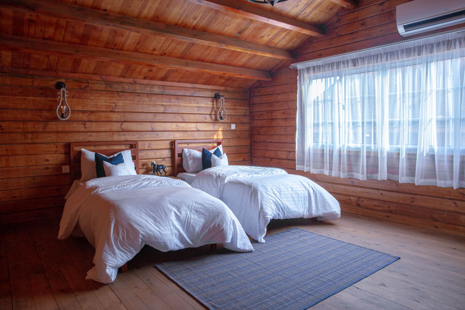 Chambre aux murs en bois avec deux lits jumeaux et linge blanc, grande fenêtre voilée