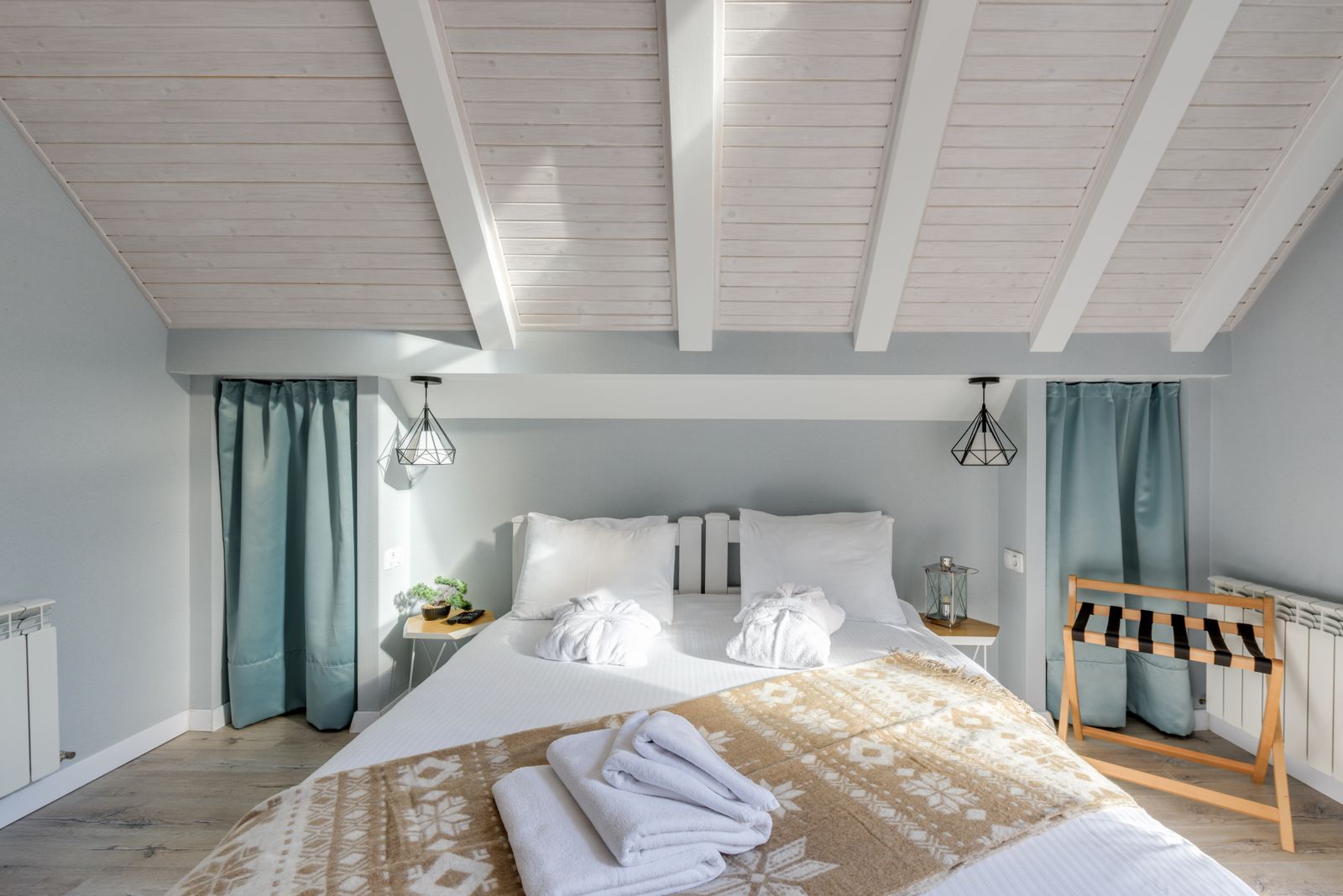 Chambre lumineuse aux rideaux bleu-gris, lit avec plaid scandinave et serviettes pliées