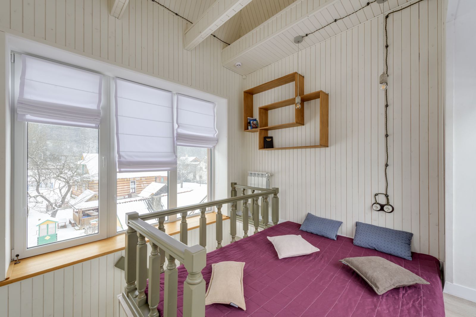 Chambre mansardée aux murs de bois clair, lit à couverture prune, vue enneigée par la fenêtre