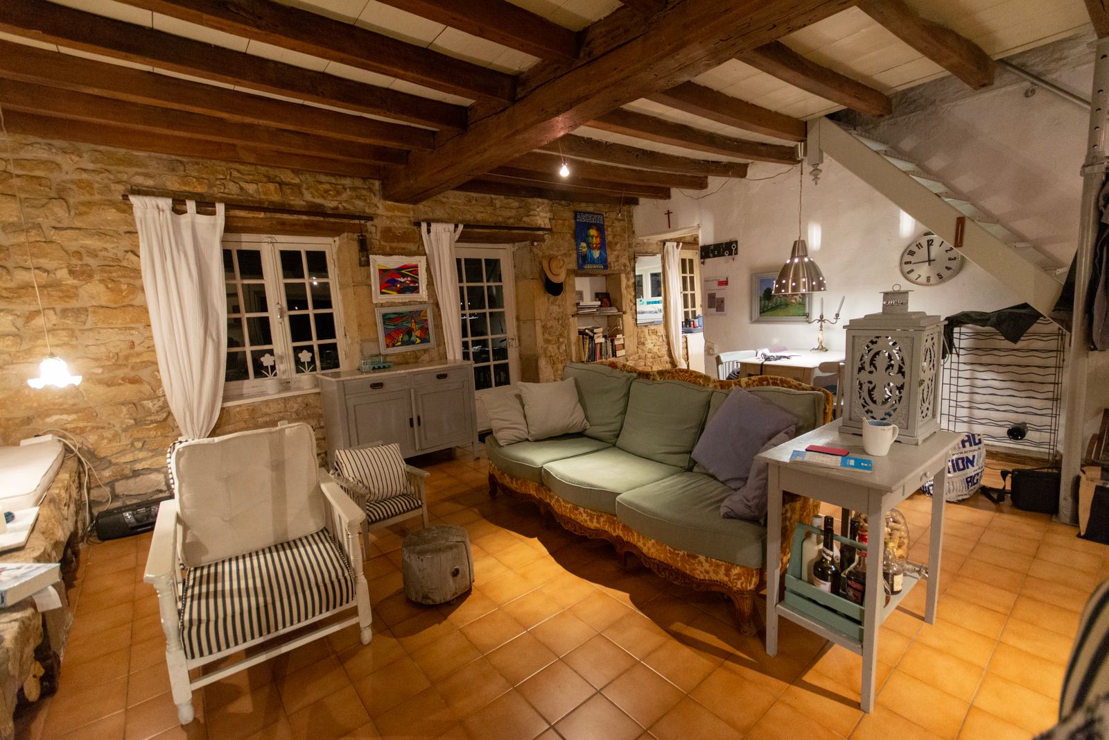 Salon aux tomettes et poutres, canapé vert et fauteuils blancs, fenêtres à petits carreaux