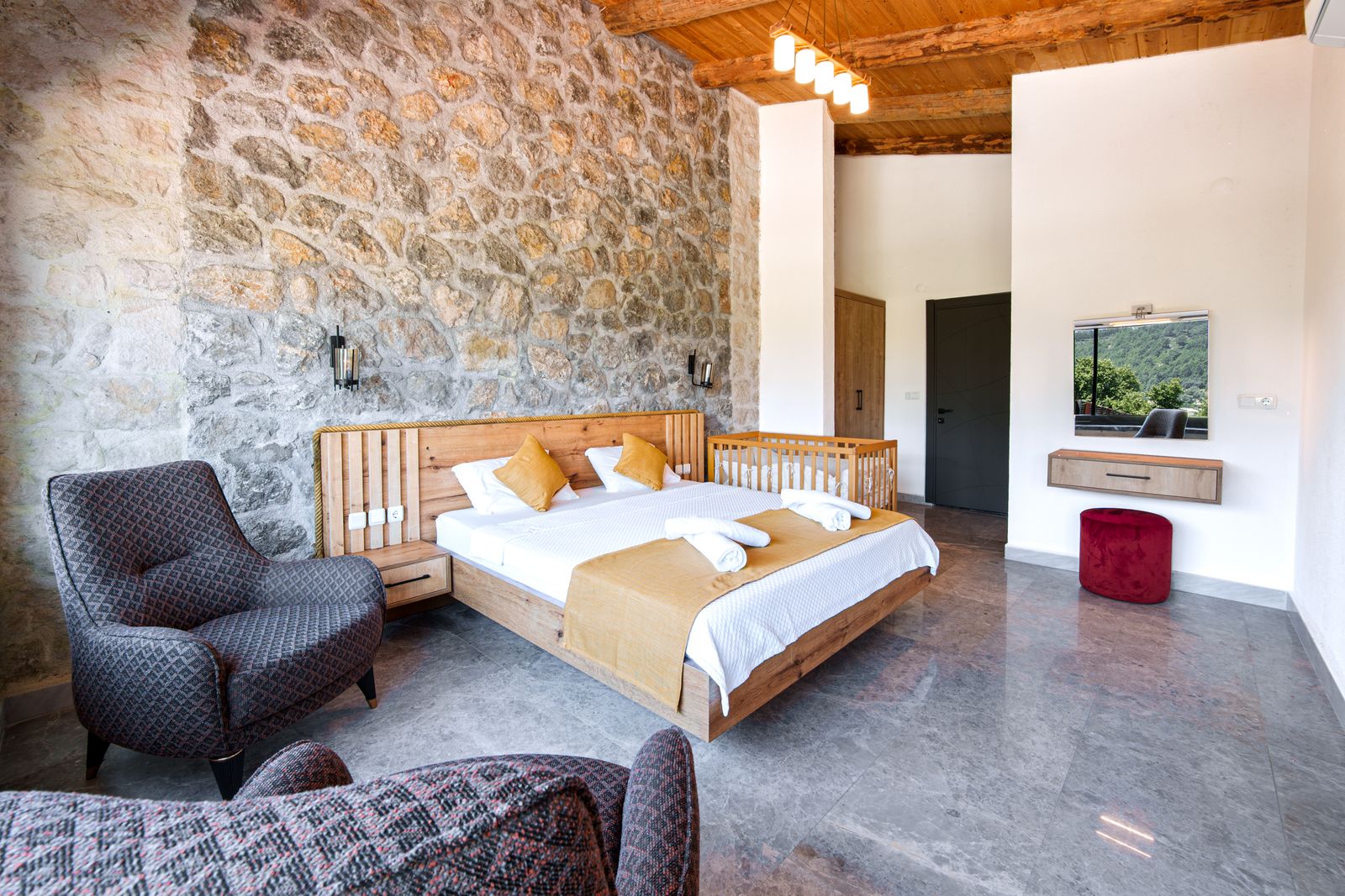 Chambre au mur de pierre apparente, lit double en bois clair et fauteuils
