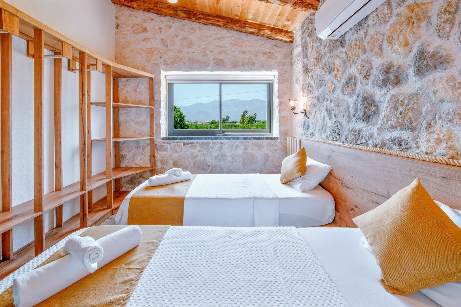 Chambre lumineuse au mur de pierre, lit blanc et fenêtre ouverte sur la campagne
