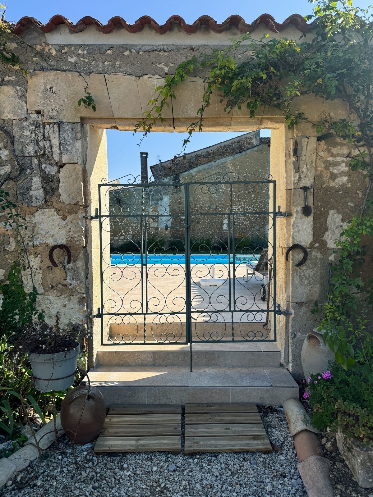 Porche en pierre et grille en fer forgé ouvrant sur la piscine
