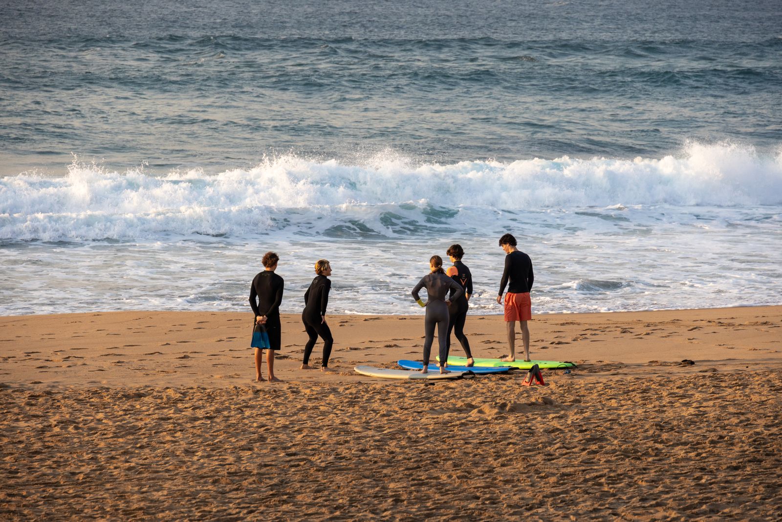 Petit groupe d’adultes en combinaison autour des planches sur le sable, avant le cours