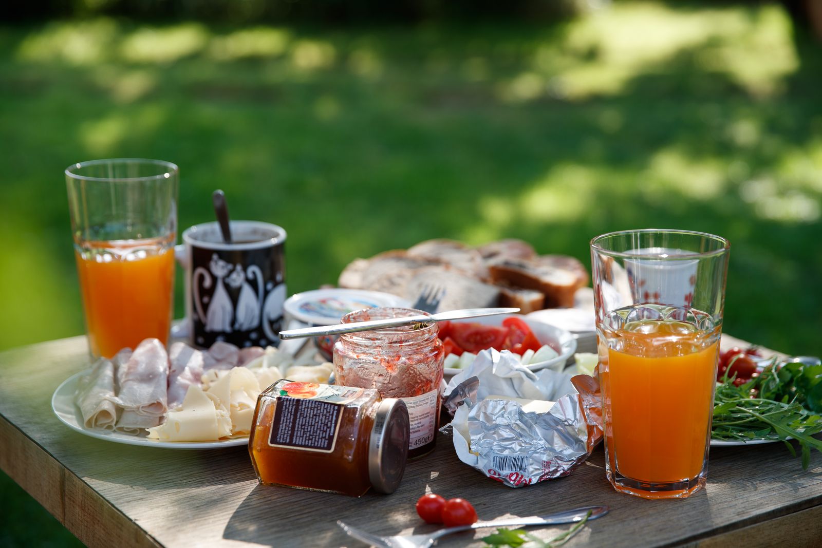 Petit-déjeuner dehors : jus d’orange, fromages et confitures sur une table en bois