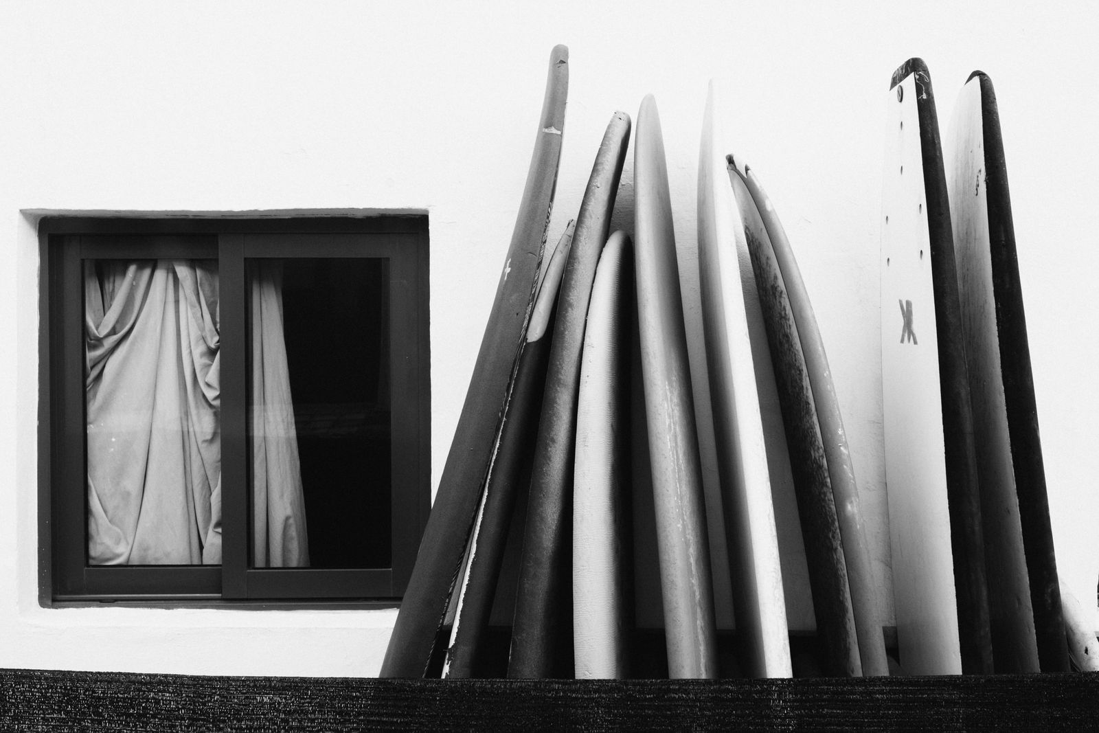 Planches de surf alignées contre un mur blanc, en noir et blanc