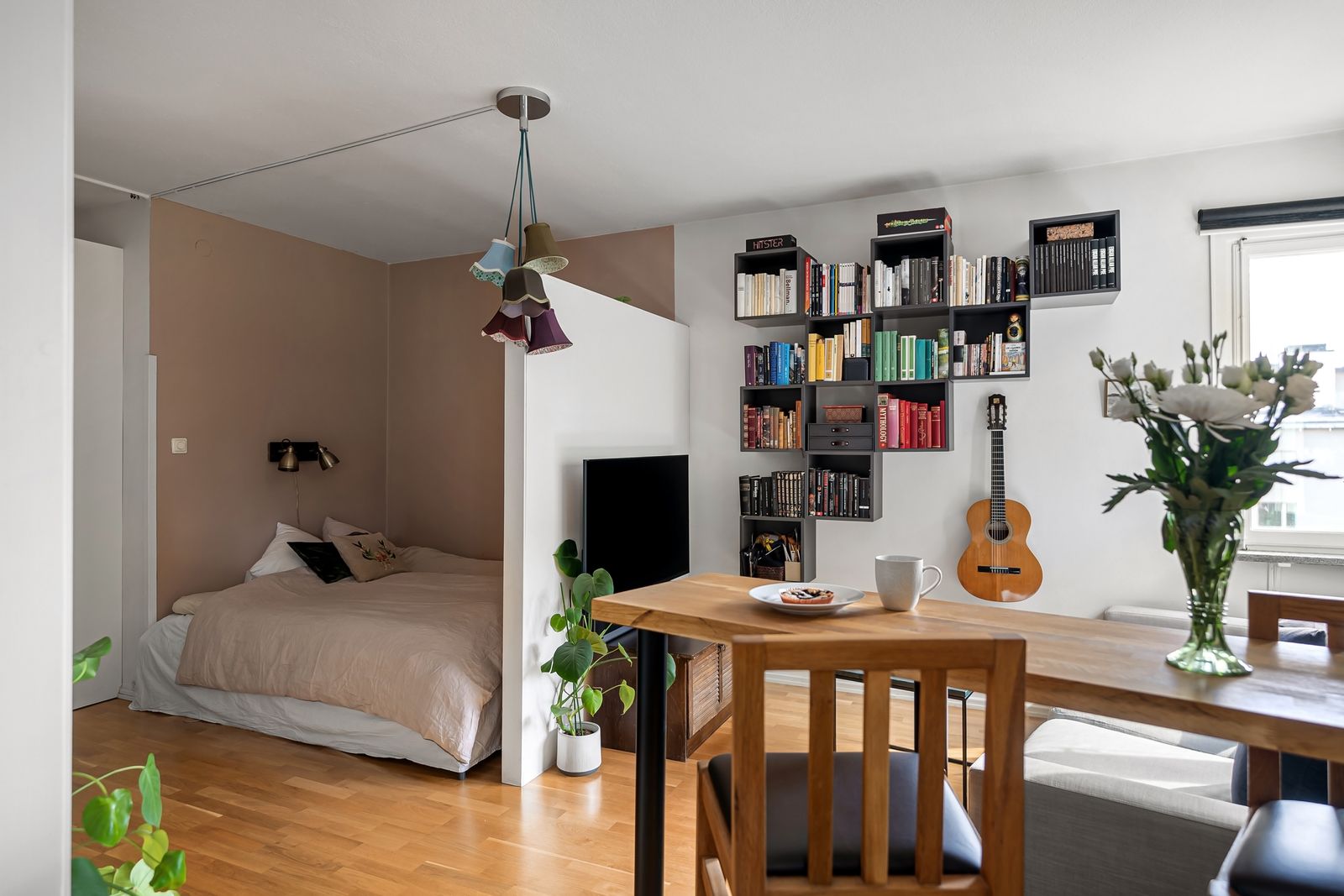 Studio au parquet clair : coin nuit, bibliothèque murale et table en bois