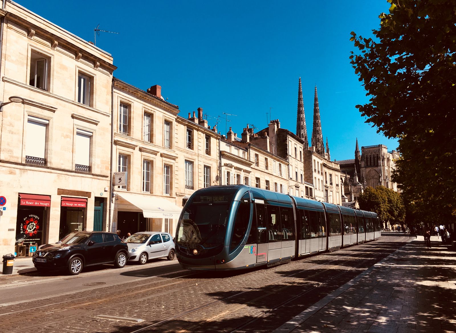 Tram dans une rue de Bordeaux bordée d’immeubles en pierre, flèches de la cathédrale au fond
