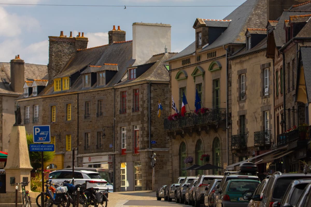 Rue commerçante d'un centre-ville breton : maisons en pierre, toits d'ardoise et drapeaux français