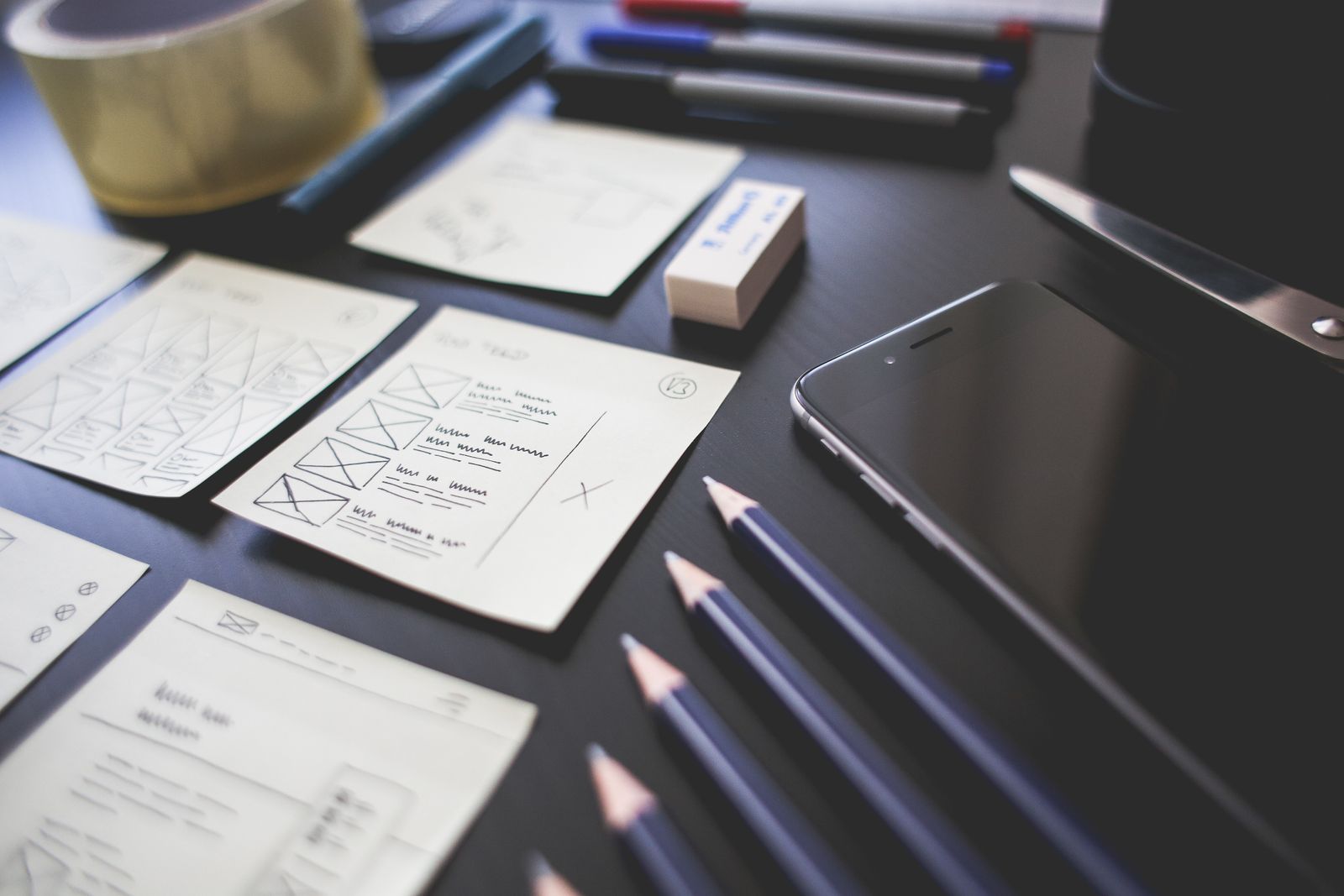 Maquettes d’écrans sur papier et crayons sur un bureau sombre