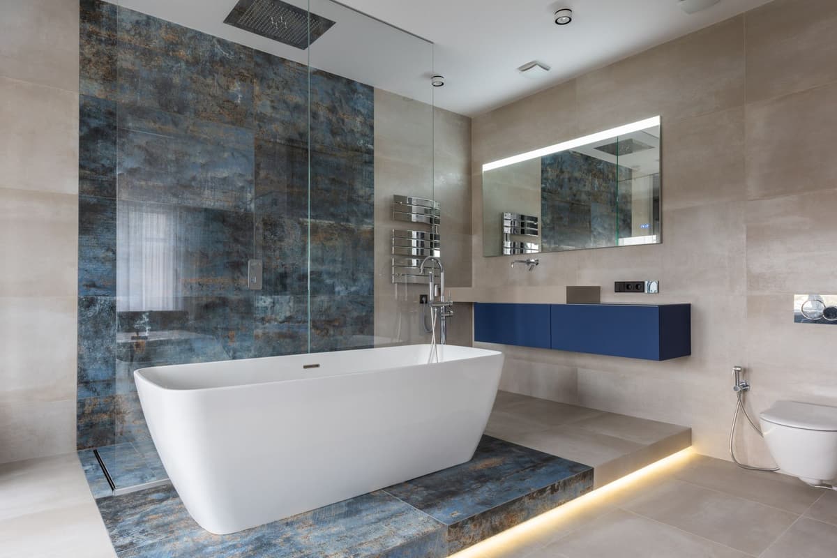 Baignoire îlot blanche devant un mur d'ardoise bleue, meuble vasque bleu nuit et sol carrelé