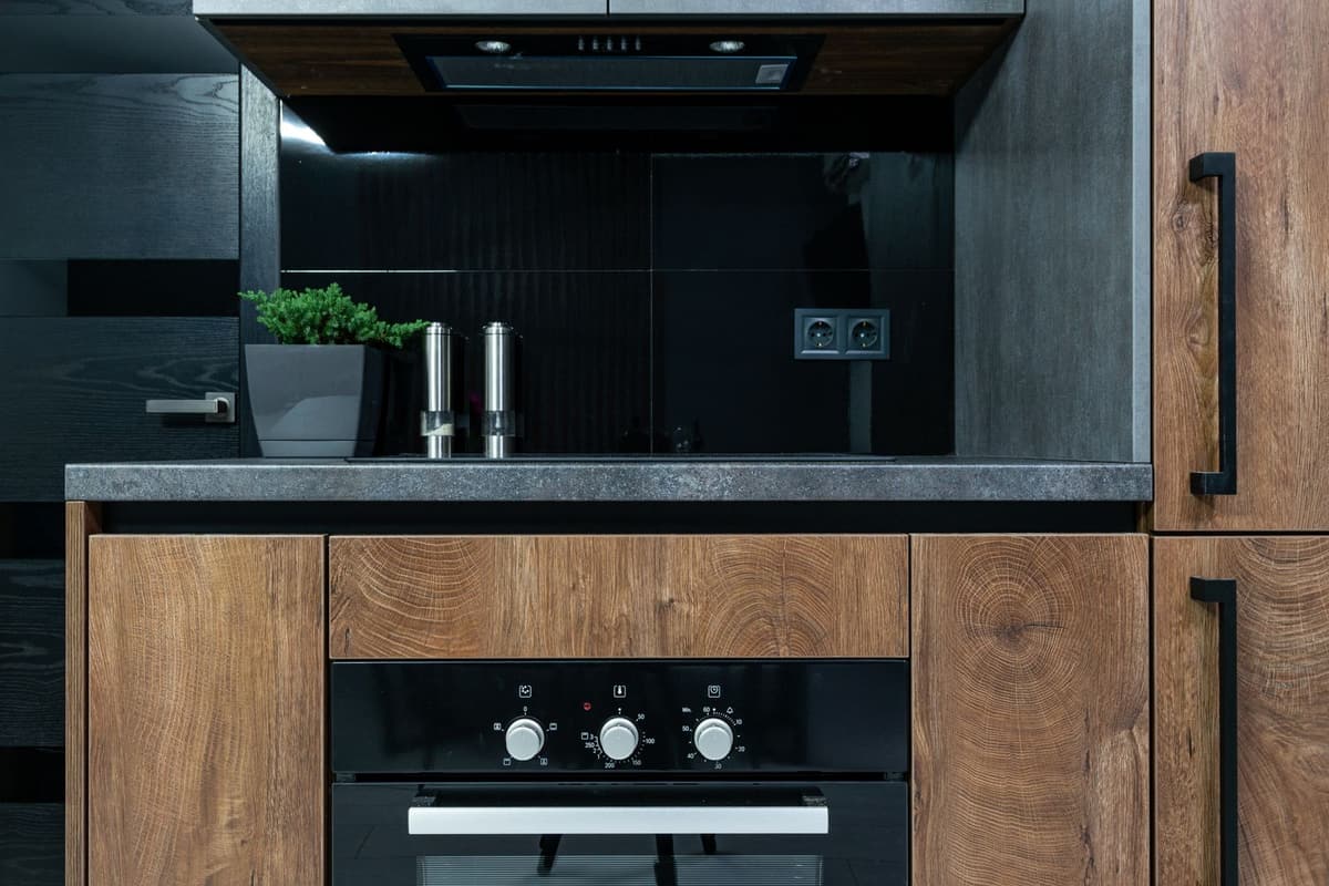 Cuisine contemporaine en bois foncé avec four encastré, plan de travail sombre et éclairage intégré