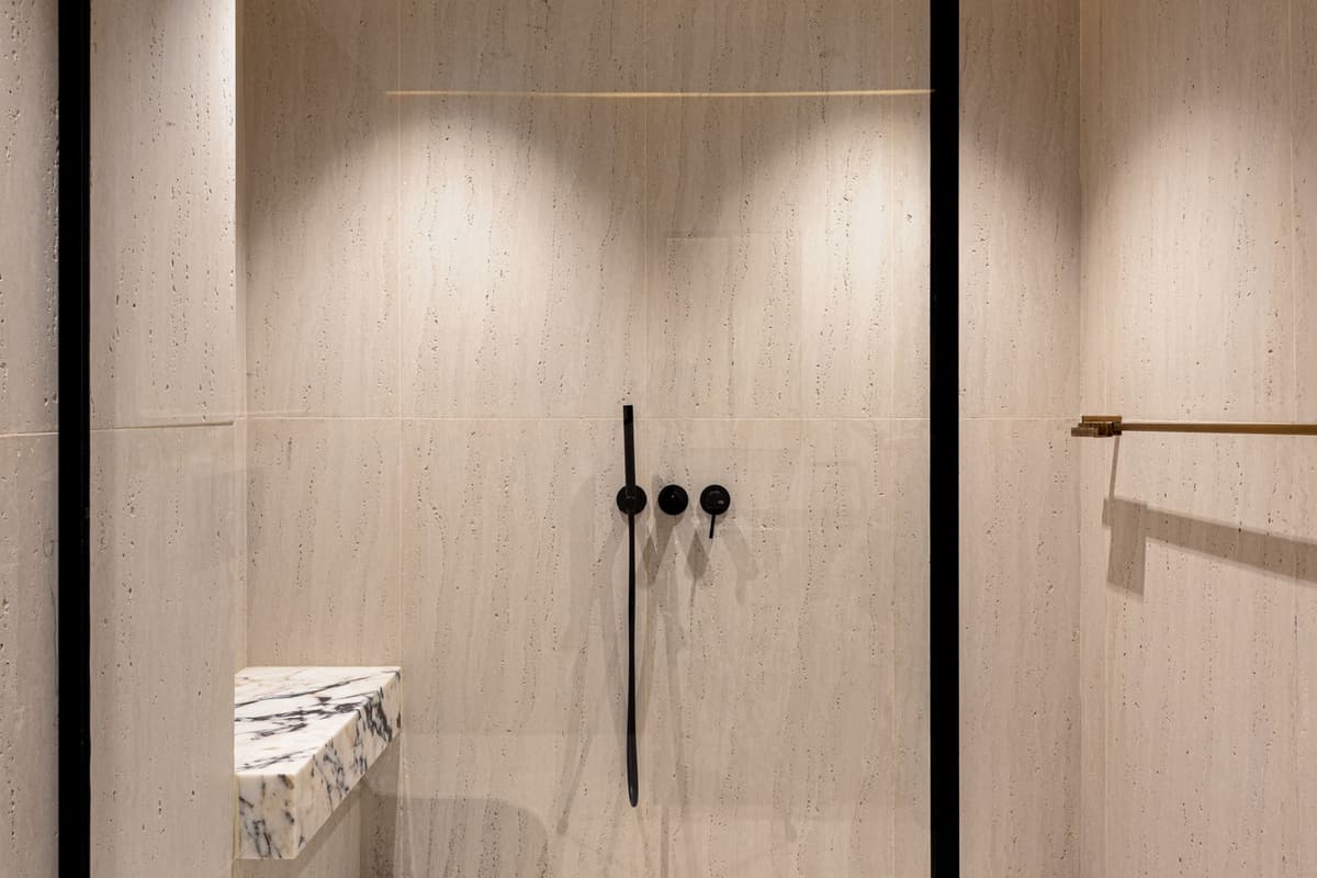 Douche à l'italienne épurée en pierre beige avec robinetterie noire et paroi vitrée